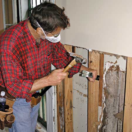 Norm taking a hammer and chisel to a mold-damaged wall