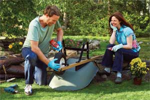 man lubricating wheelbarrow while woman with pruners looks on