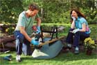 man lubricating wheelbarrow while woman with pruners looks on