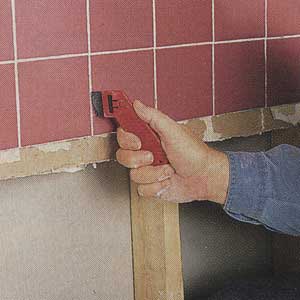 Scratching out existing grout from between ceramic tiles with a grout saw.