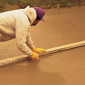 Using a 2x4 as a guide, control joints are cut with a jointer, which resembles a trowel with a blade in the center. At this point the concrete is firm enough to support some weight but still wet enough to be worked. The joints, which divide the drive into six-by-eight-foot squares, give the concrete a place to expand and contract. The idea here is that the concrete will crack along the joints and not in the middle of the slab. If cracks do form elsewhere (usually due to shifting soil or an inadequate base), they must be patched to prevent water from working its way into the concrete and spalling it. 