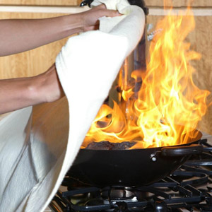 a woman stopping the stovetop fire with a blanket