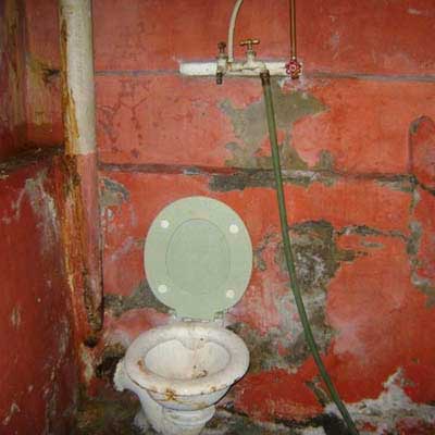 a toilet in a basement sitting underneath a hose spigot