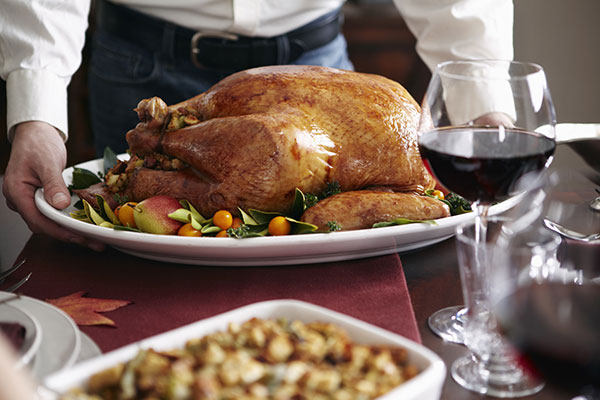 people standing behind a thanksgiving themed table laden with turkey wine and side dishes