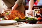 people standing behind thanksgiving themed table ladden with turkey wine and more