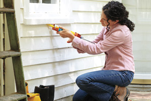 woman caulking window for energy efficiency