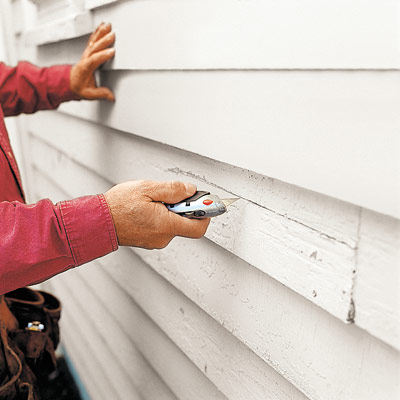 man cutting damaged clapboard with utility knife