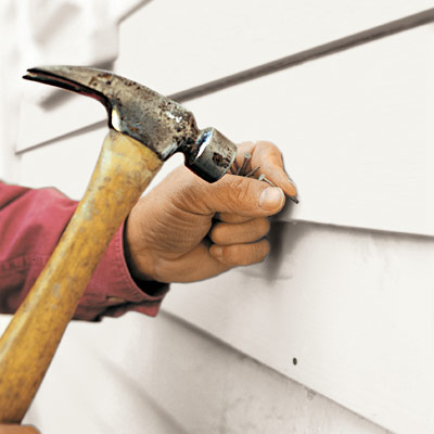 man fastening replacement clapboard to house exterior