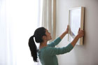woman hanging a framed picture on a wall