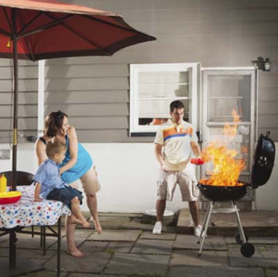 woman and child afraid as man adds lighter fluid to flaming grill 