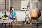 woman and child are afraid as man adds lighter fluid to flaming grill