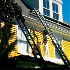 person on scaffold painting exterior of house yellow