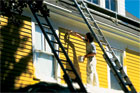 person on scaffold painting exterior of house yellow