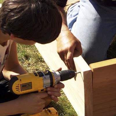 boy using a cordless driver to attach 2x10 cedar boards with deck screws