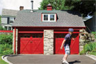 skateboarder rolling downhill from a garage with two red, carriage-style doors