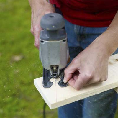 hands using a jigsaw to cut a wood board to shape for the box, top or legs of the pet ramp