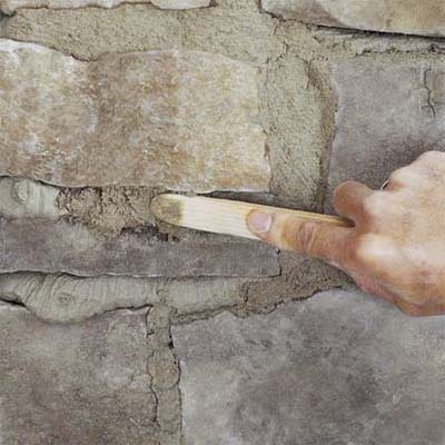 a hand using a striking tool to carve the grout when creating a stone veneer fireplace surround