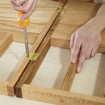 hands attaching hinges to connect the sections of the a dog gate