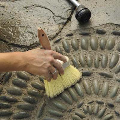Mark Powers using a stiff-bristled brush to dress and shape the joints of his pebble mosaic