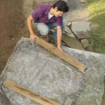 Mark Powers covers his pebble mosaic with a plastic tarp weighed down by 2 4x4s in order to cure the finished mosaic