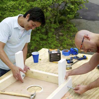 two men attaching legs for cornhole game board