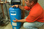 plumbing and heating expert richard trethewey crouched before a newly installed water pressure booster
