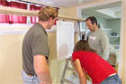 kevin o'connor watching as a suspended kitchen cabinet door is painted
