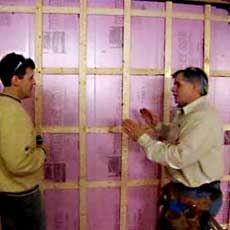 Tom Silva holding up an insulating panel in a basement corner wall