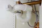 a hand under a kitchen sink underlines a replaced PVC sink trap