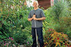 This Old House editor, Scott Omelianuk standing in a gravel walkway through a garden holding a rake