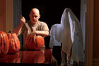 TOH editor, Scott Omelianuk carves a pumpkin with a large knife with a person wrapped in a sheet behind him